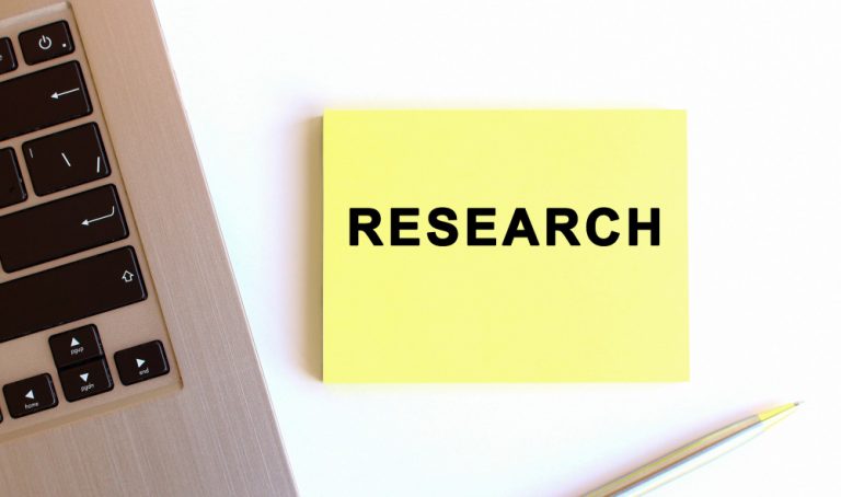 Photo of laptop with yellow sticky note with the word "research" on it.