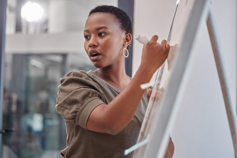 Young Black woman with short hair writing on a whiteboard at work