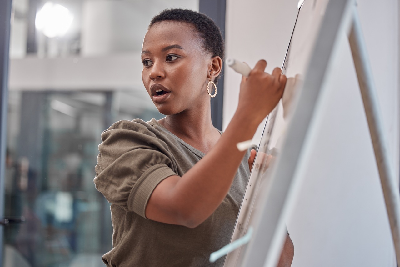 Young Black woman with short hair writing on a whiteboard at work